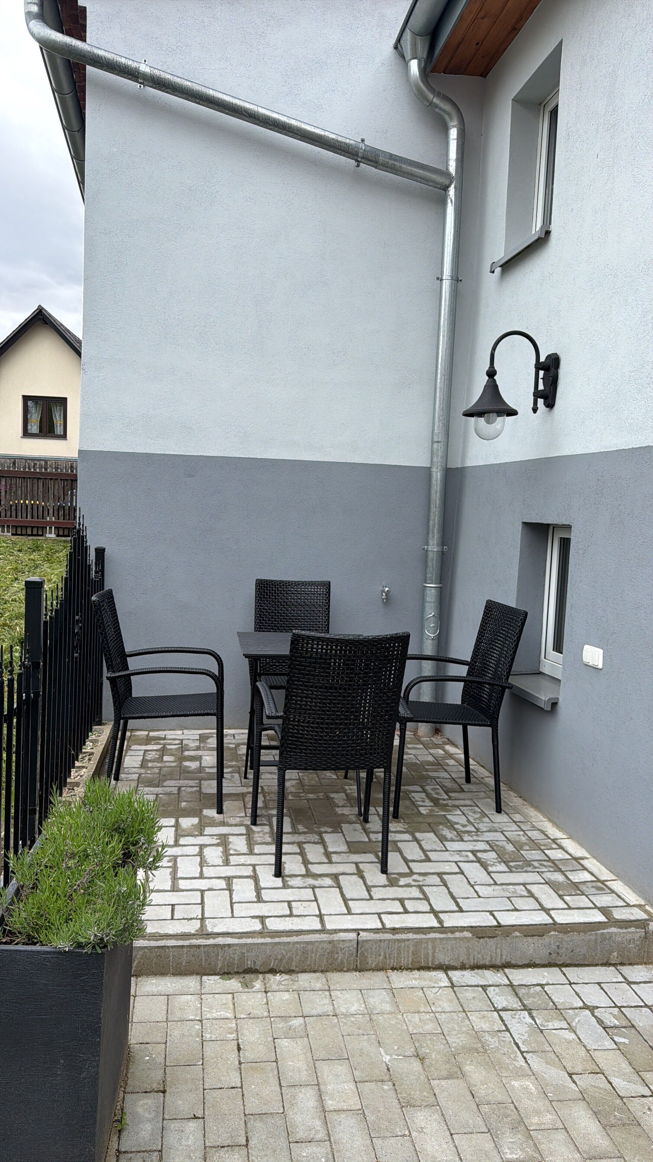 Une terrasse extérieure avec une table et des chaises, une clôture en métal noir et un mur de bâtiment gris.