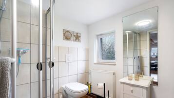 Un baño con ducha, inodoro, tocador y un espejo grande.