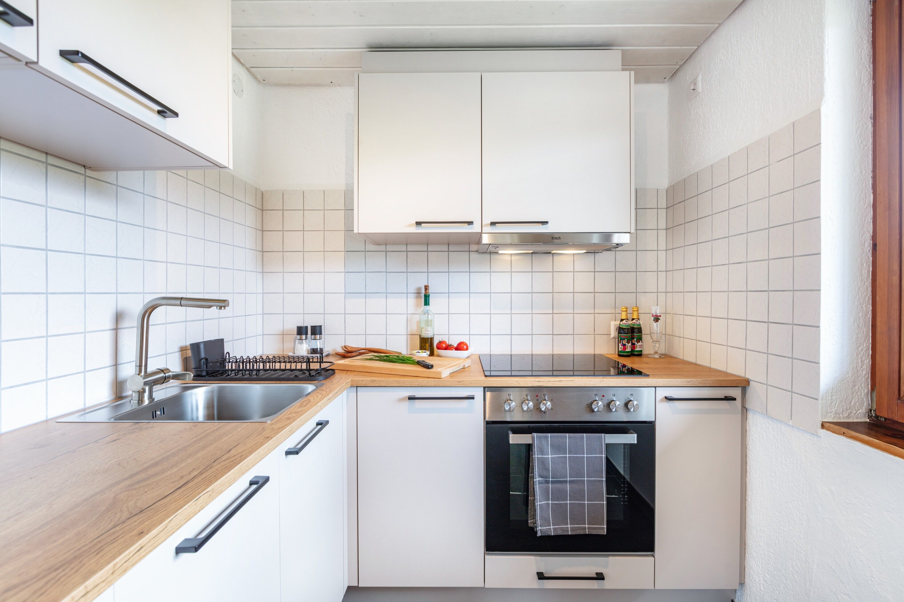 A compact kitchen with white cabinets, a wooden countertop, a stainless steel sink, and a built-in oven.