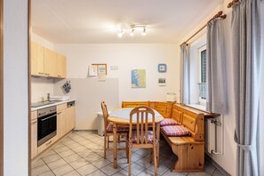 Une cuisine de taille réduite avec des meubles en bois, une table à manger avec des chaises, un banc et une fenêtre avec des rideaux.