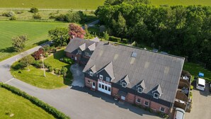 A large building with a sloped roof, surrounded by green fields and a body of water. - Apartment 'Fereinhof Paulsen - Lachmöwe' with Private Terrace, Shared Garden and Wi-Fi (Pellworm)