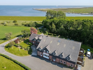A large building with a sloped roof, surrounded by green fields and a body of water.
