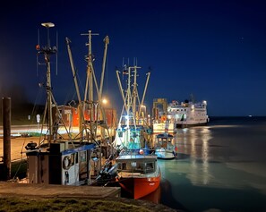 A harbor at night with boats docked, a large ship in the background, and a building with visible windows. - Apartment 'Fereinhof Paulsen - Lachmöwe' with Private Terrace, Shared Garden and Wi-Fi (Pellworm)