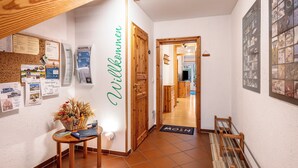 A hallway with a welcome sign, a bulletin board with notices, a wooden bench, and a door leading to a kitchen. - Apartment 'Fereinhof Paulsen - Lachmöwe' with Private Terrace, Shared Garden and Wi-Fi (Pellworm)