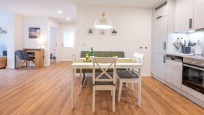A modern kitchen with white cabinets, a dining table with chairs, and a hanging pendant light. - Apartment 'Ferienhof Paulsen - Seeschwalbe' with Private Terrace and Wi-Fi (Pellworm)