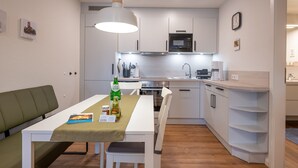 A modern kitchen with white cabinets, a microwave, and a dining area with a table and chairs. - Apartment 'Ferienhof Paulsen - Seeschwalbe' with Private Terrace and Wi-Fi (Pellworm)