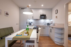 Cozinha moderna com armários brancos, micro-ondas e área de refeições com mesa e cadeiras.
