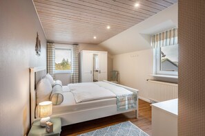 Et soveværelse med seng, natbord, lampe og et vindue med gardiner.
