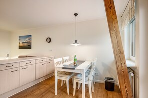 Une cuisine moderne avec des meubles blancs, une table à manger avec des chaises, un luminaire suspendu et une fenêtre avec des stores.