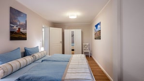Una camera da letto con due letti, un armadio bianco, una piccola sedia bianca e due quadri alle pareti.