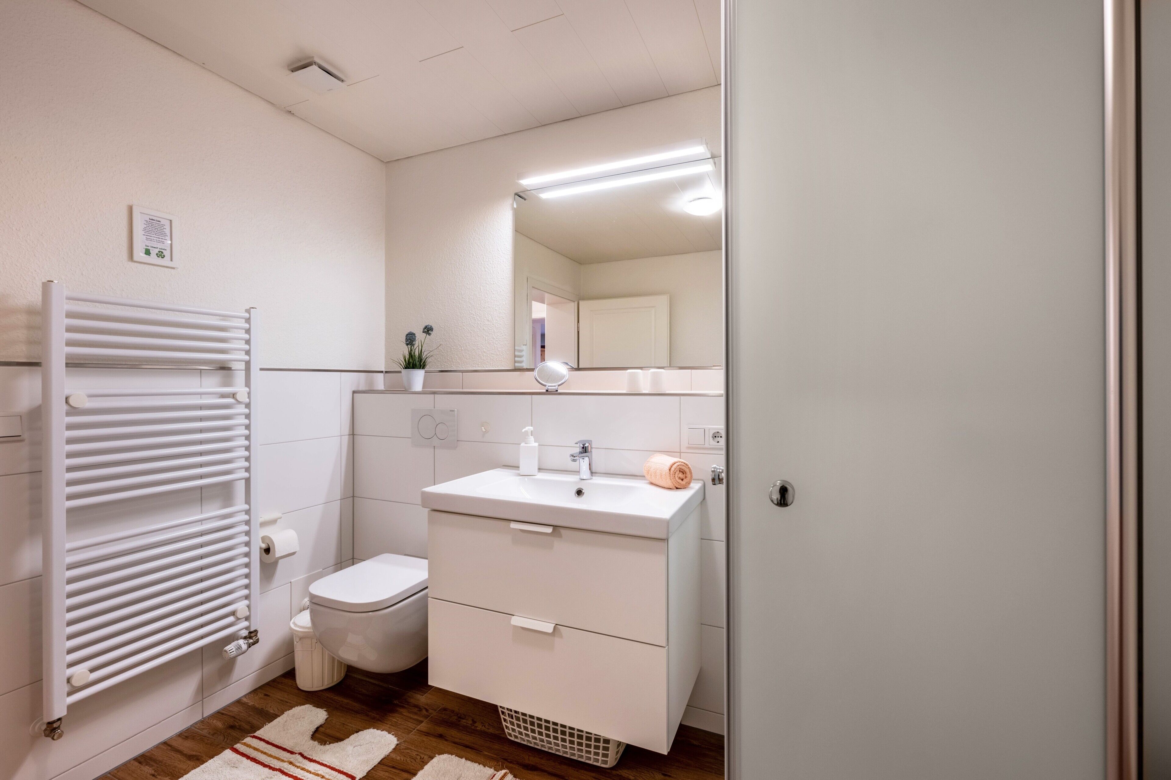 A modern bathroom with a white radiator, toilet, sink, and mirror.