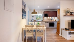 Una cucina moderna con mobili in legno, un'area pranzo con tavolo e sedie bianche e un televisore su un supporto in legno.