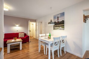 Ein Zimmer mit einer roten Couch, einem weißen Tisch und einer Essecke mit weißen Stühlen.