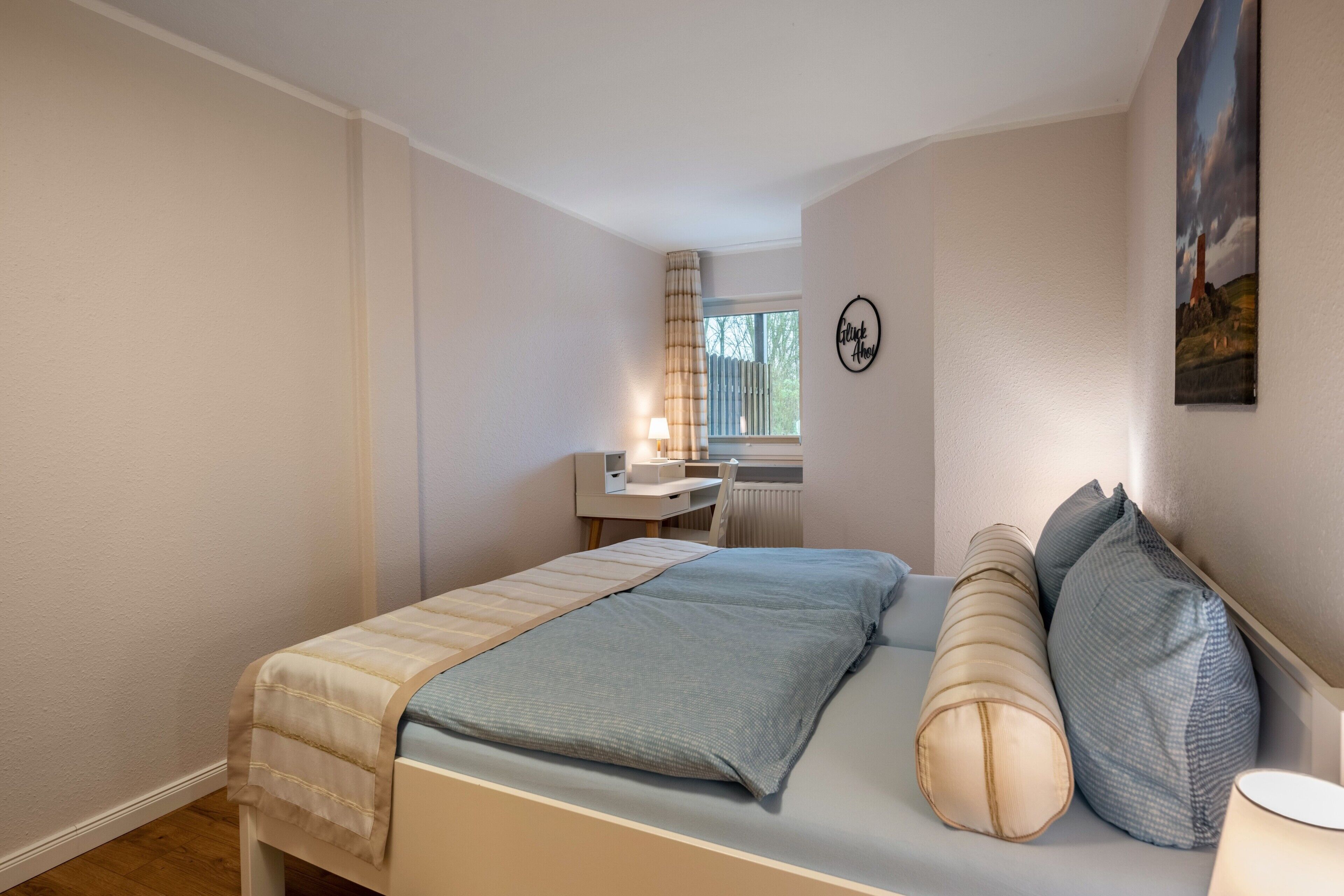 Ein Schlafzimmer mit Bett, Nachttisch, Lampe und einem Fenster mit Vorhängen.