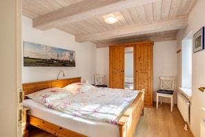 Une chambre à coucher avec un lit en bois, une armoire en bois, une chaise et un tableau accroché au mur.
