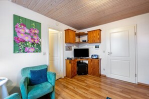 Une pièce comprenant un fauteuil de couleur turquoise, des meubles en bois, un téléviseur à écran plat et un réfrigérateur.