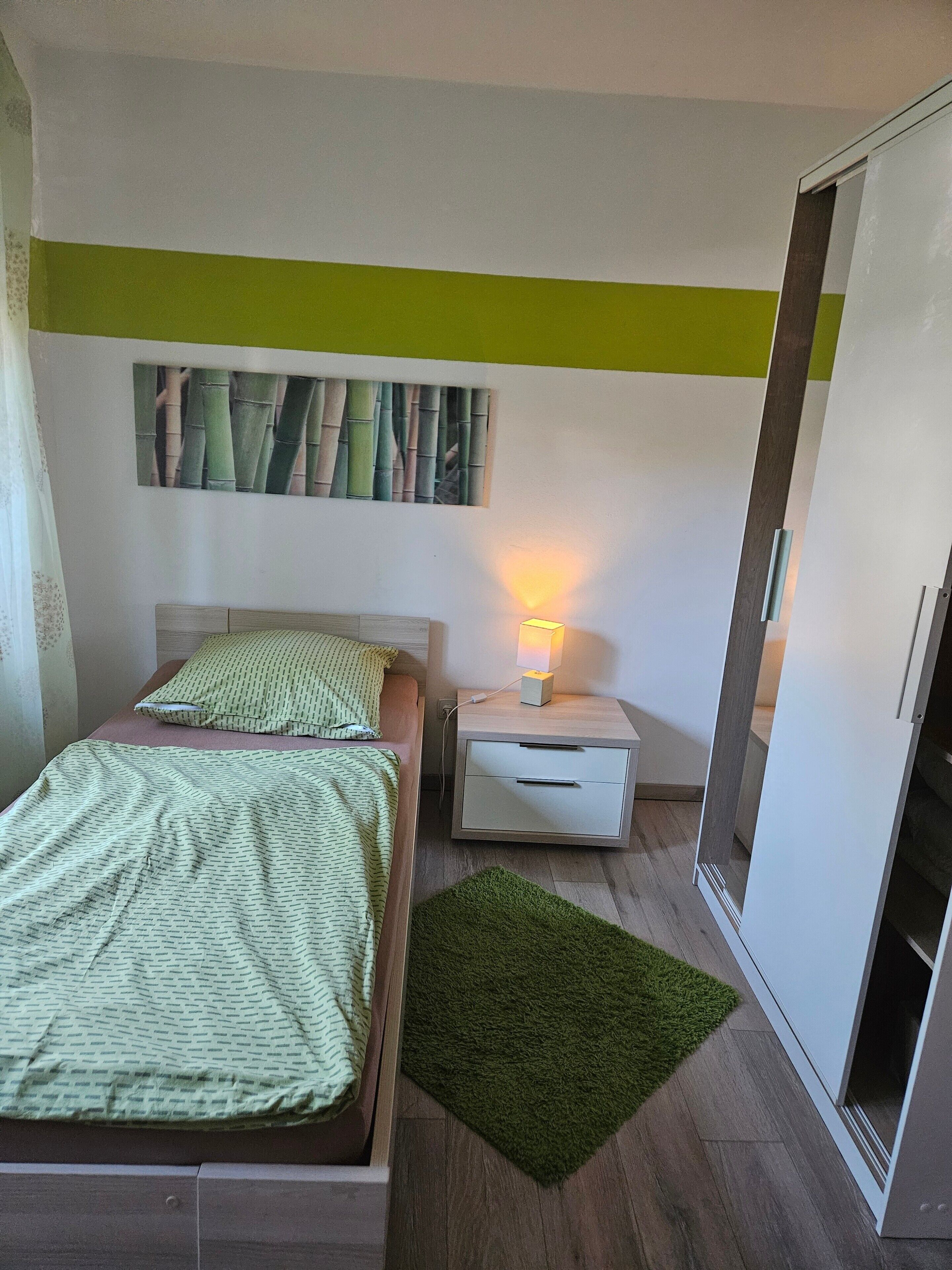 Une chambre à coucher avec un lit, une table de chevet avec une lampe, une armoire et un tapis vert.