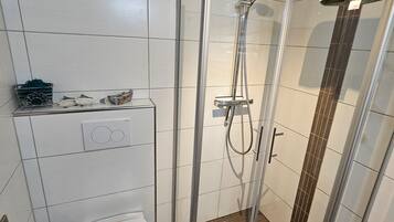 Een moderne badkamer met een glazen douchecabine, toilet en handdoekhouder.