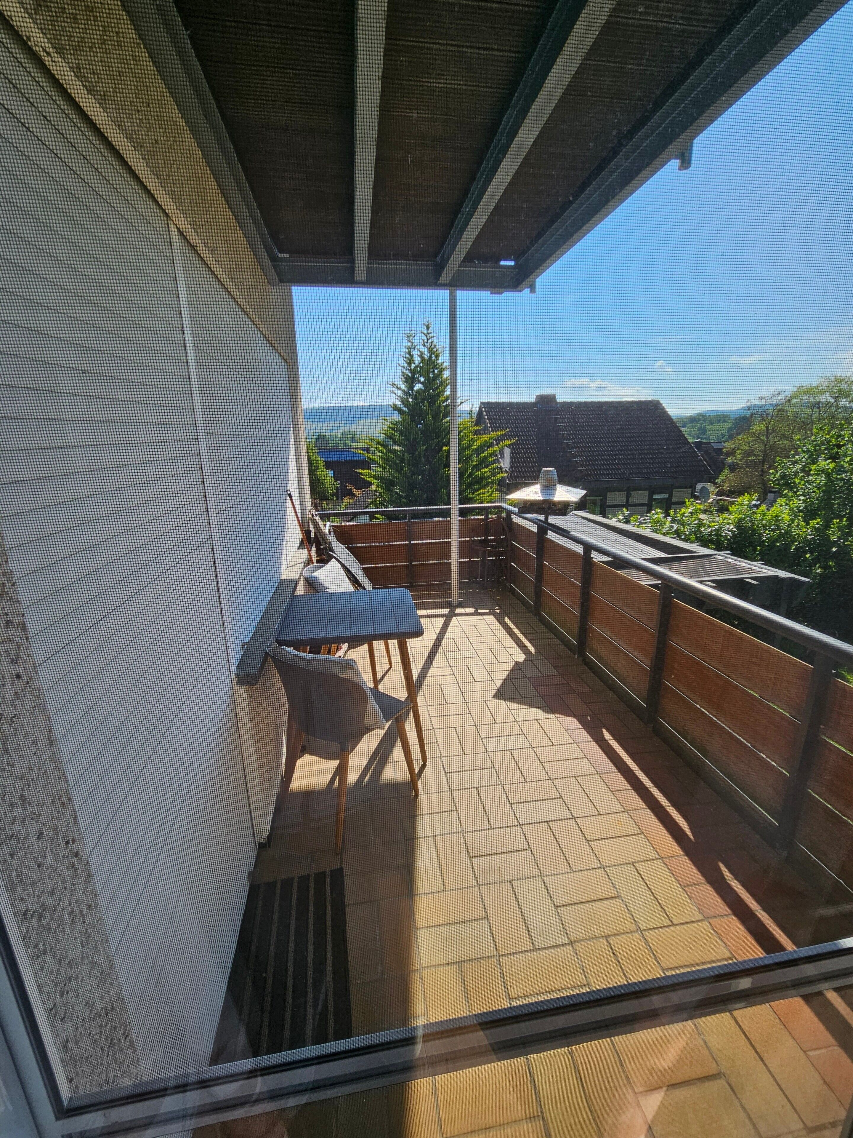 A balcony with a view of a house, a chair, and a table.