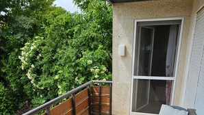 Eine überdachte Terrasse mit gefliestem Boden, einem Holzzaun und einem Tisch mit Stühlen.