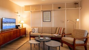 Een woonkamer met een bank, twee fauteuils, een salontafel, een televisie en een lamp.