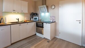 Een kleine keuken met witte kasten, een magnetron, een fornuis en een klok aan de muur.