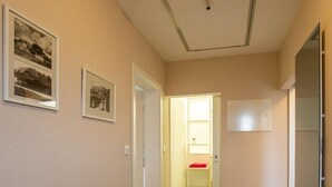 Een hal met een houten vloer, een zwart tapijt, beige wanden en twee ingelijste foto's.