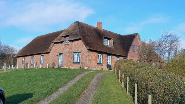 Een groot, wit vakantiehuis met rieten dak, veel ramen en een verzorgd gazon.