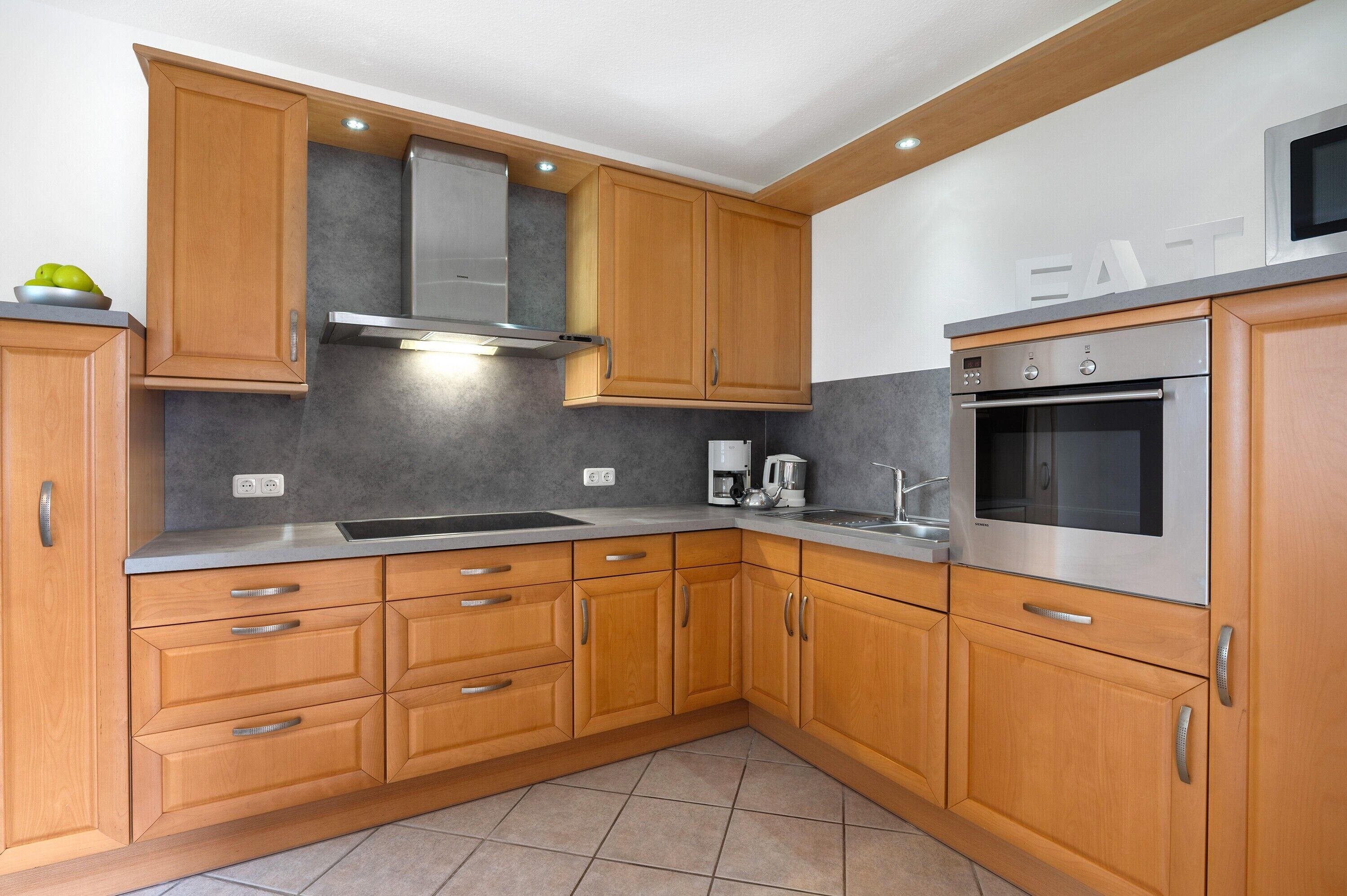 A modern kitchen with wooden cabinets, stainless steel appliances, and a grey backsplash.