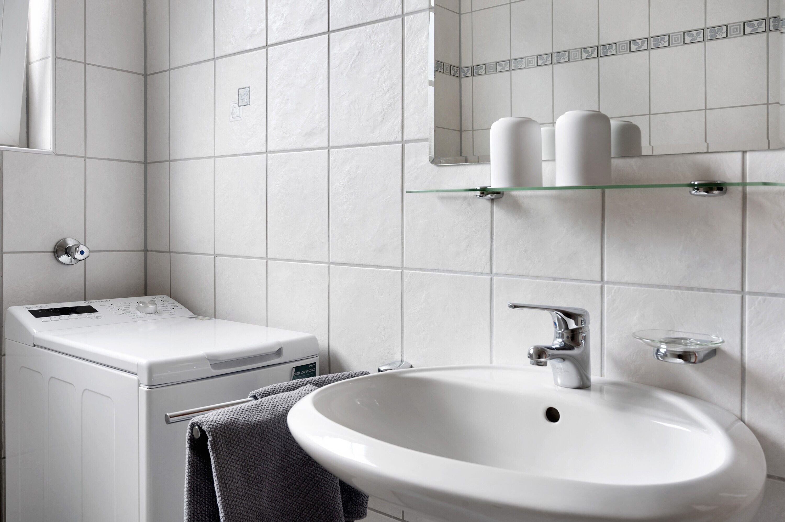 Ett badrum med ett vitt handfat, en spegel och en tvättmaskin.