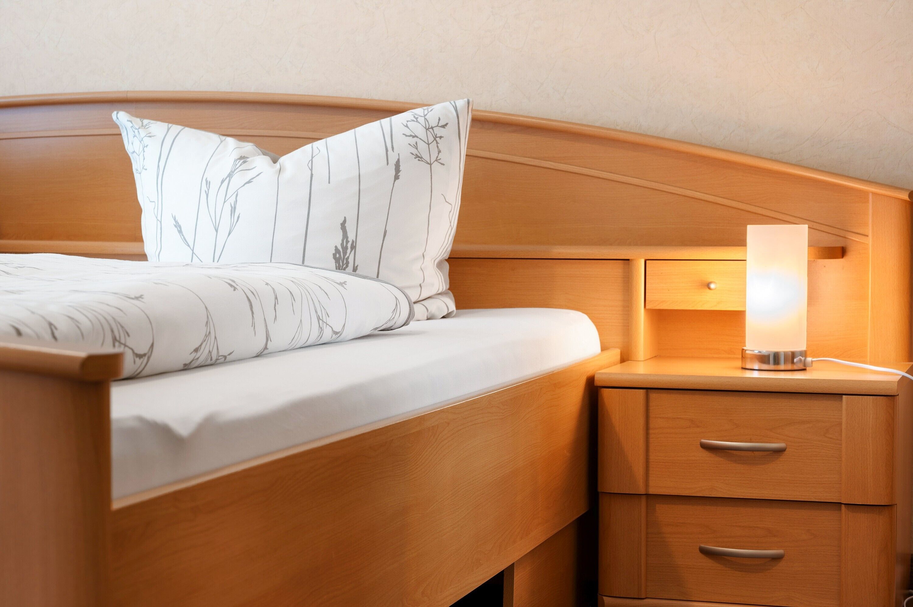 A bed with a headboard, a bedside lamp, and a wooden nightstand with drawers.