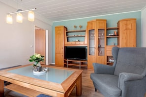 Ein Wohnzimmer mit Couchtisch aus Glas, einer grauen Couch, Holzschränken und einem Flachbildfernseher.