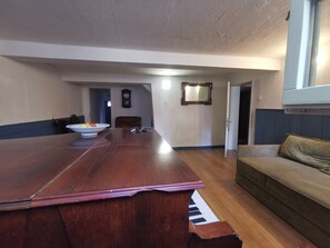 A spacious living area with a long wooden table, a couch, a piano, and a dining table with a bowl and keys. - Holiday Apartment "Wohnen Im Denkmal" with Mountain View & Wi-Fi (Langenburg)