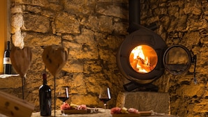 Un mur de pierres, un poêle à bois, une bouteille de vin et des verres sur une table.
