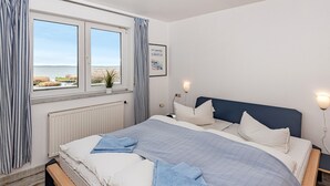 A bedroom with a large bed, a view of the sea, a window with curtains, and a bedside lamp.