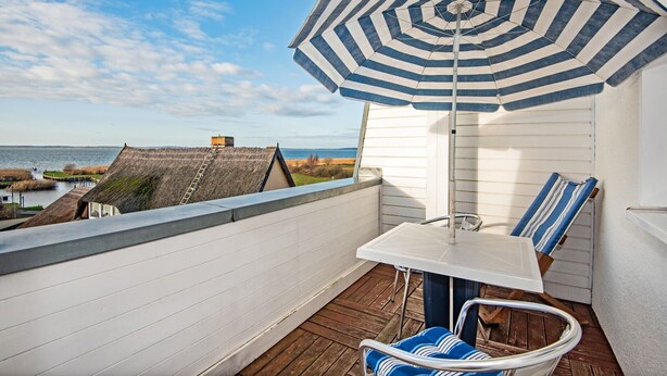 A balcony with a view of the sea, a striped umbrella, and a table with chairs.
