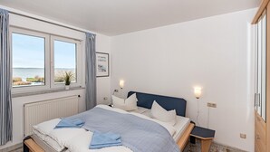 A bedroom with a bed, bedside tables, a window with curtains, a radiator, and a view of the sea. - Apartment 'Type B I 2nd Floor' with Lake View, Shared Terrace and Wi-Fi (Loddin)