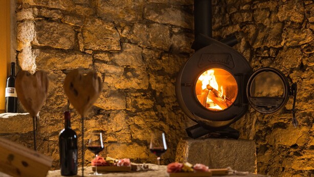 A stone wall with a wood-burning stove, a bottle of wine, and glasses on a table. - Riesling Apartment with Shared Pool, Garden, and Wi-Fi (Auggen)