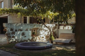 Mural de pedra, um trampolim e um banco numa área de jardim.