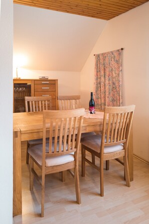 Un comedor con una mesa y sillas de madera, un aparador con copas de vino y una botella sobre la mesa.