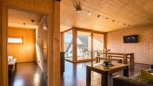 Un intérieur en bois comprenant un coin repas, un canapé, un téléviseur et une grande fenêtre.