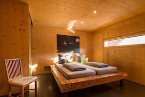 Quarto de cabana de madeira com uma cama, uma cadeira, um quadro na parede e uma janela.