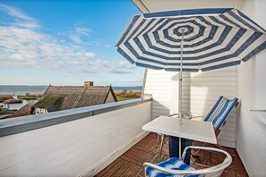 Un balcon avec vue sur la mer, un parasol rayé et une table avec des chaises.