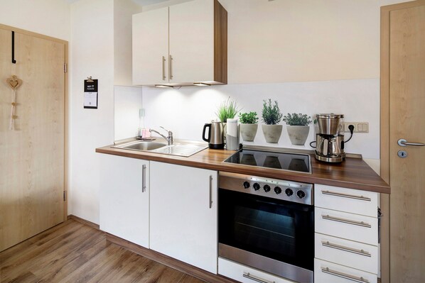 A modern kitchen with white cabinets, a stainless steel oven, a coffee maker, and potted plants.
