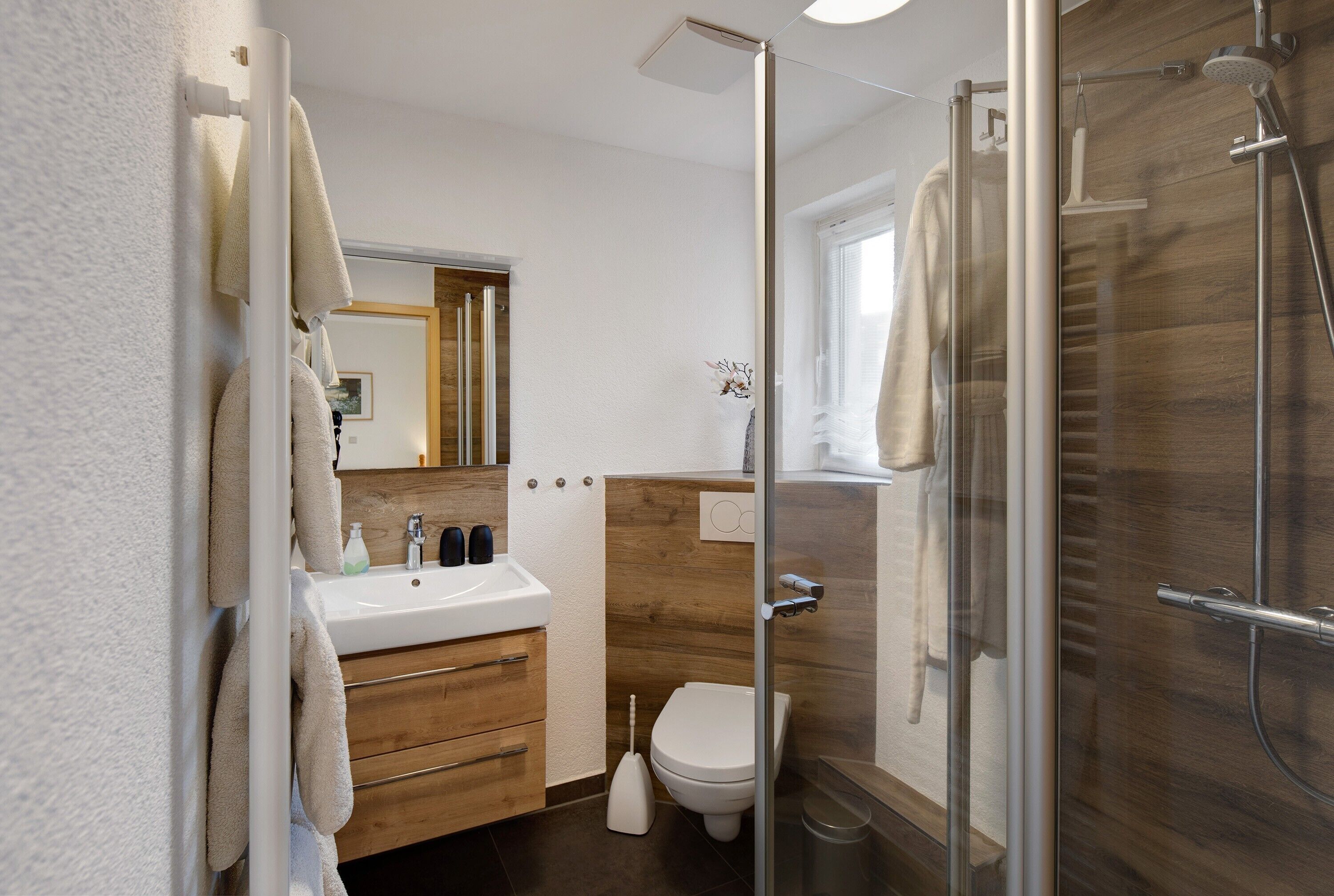 Ein modernes Badezimmer mit Duschkabine aus Glas, Waschtisch aus Holz und weißer Toilette.