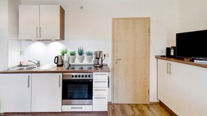 Cocina compacta con armarios blancos, horno empotrado, cafetera y televisor sobre una encimera de madera.
