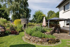 A garden with a stone wall, a patio with a table and chairs, and a covered outdoor seating area.
