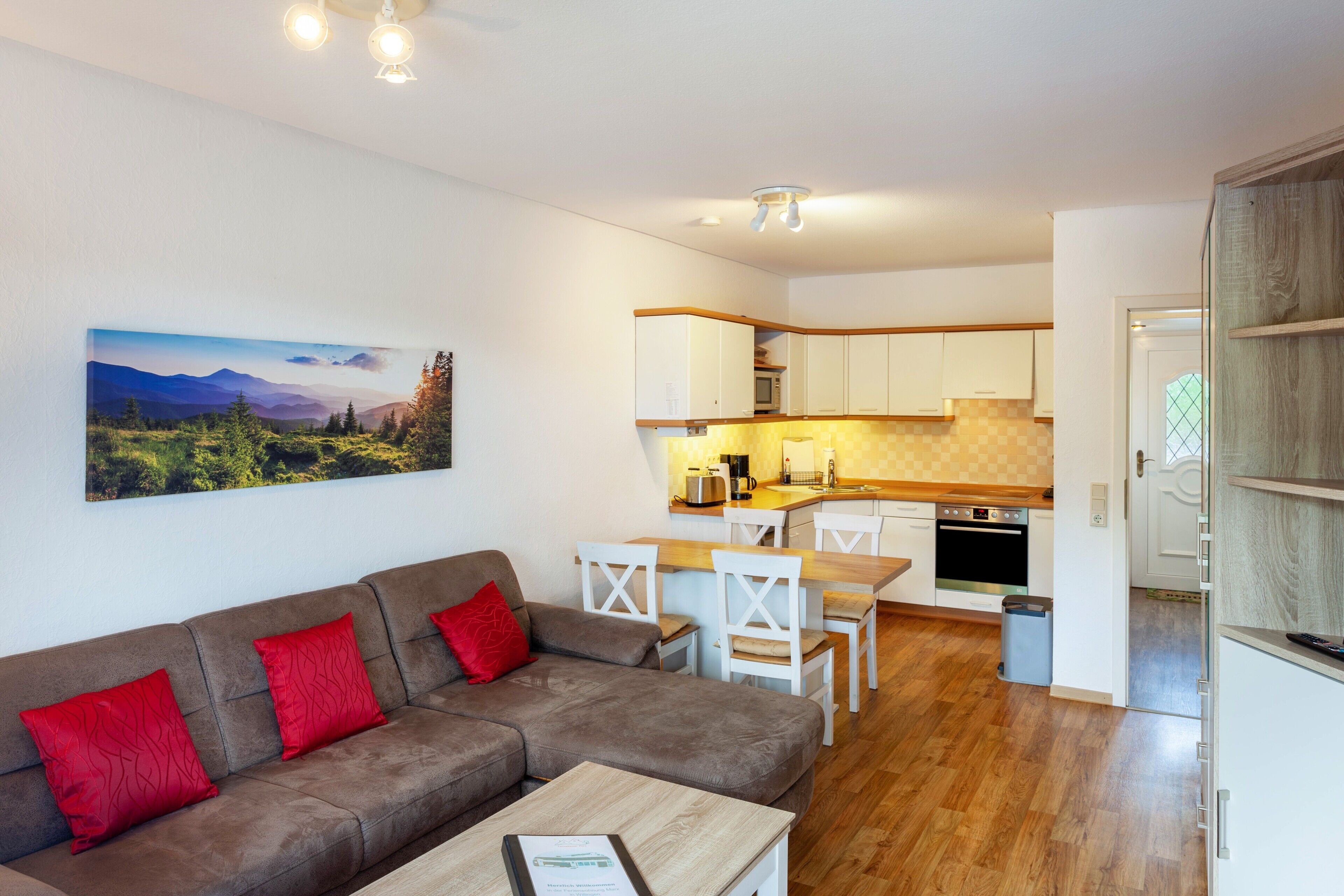 Una sala de estar moderna con un sofá, sillas, una mesa de centro y una zona de cocina con armarios y electrodomésticos.