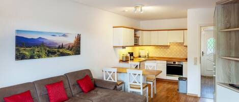 Una sala de estar moderna con un sofá, sillas, una mesa de centro y una zona de cocina con armarios y electrodomésticos.