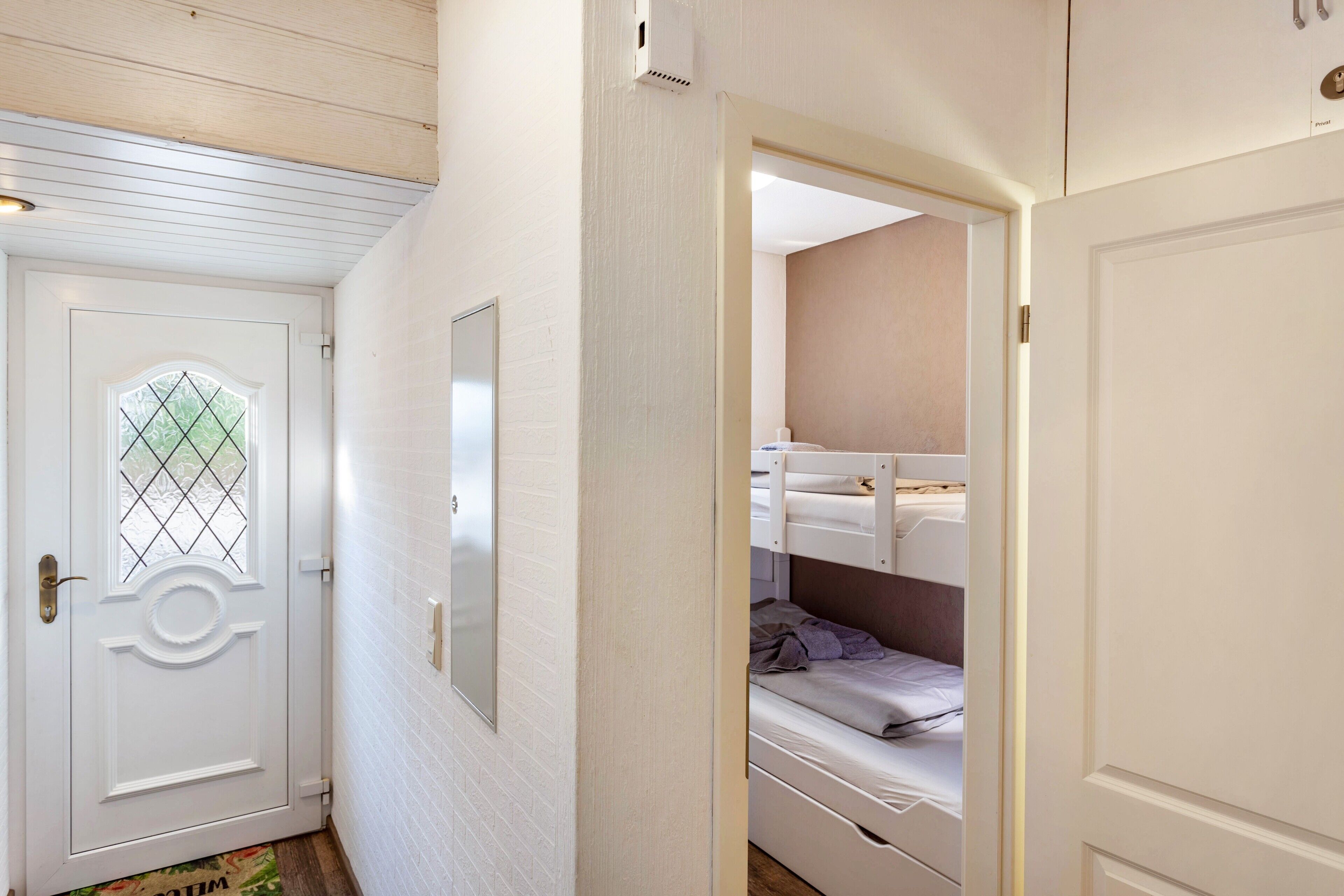 Une pièce avec une porte blanche, un miroir, un lit superposé et une petite fenêtre.